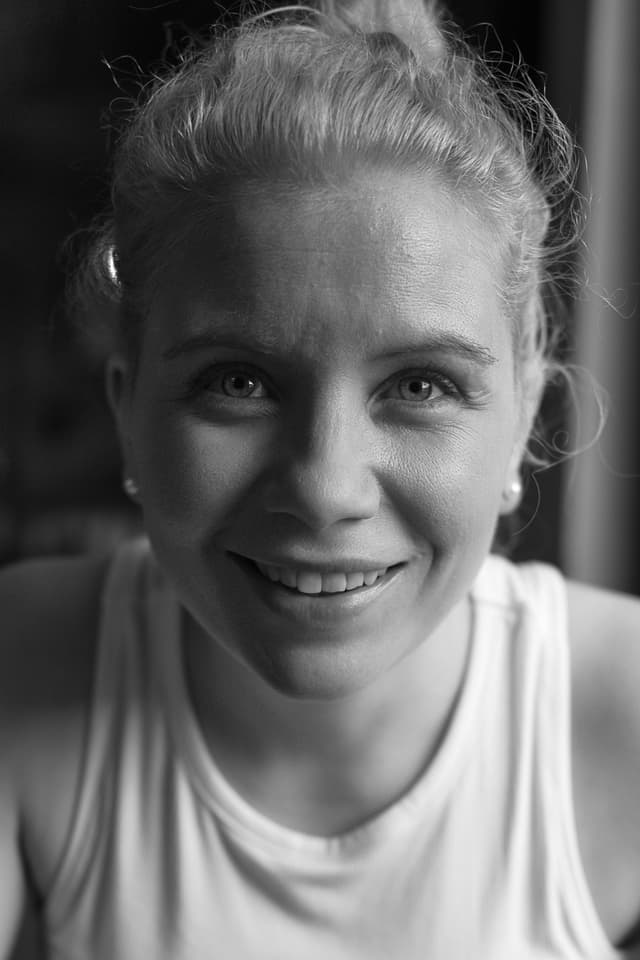 A smiling young woman with blonde hair and a warm expression, set against a dark background.