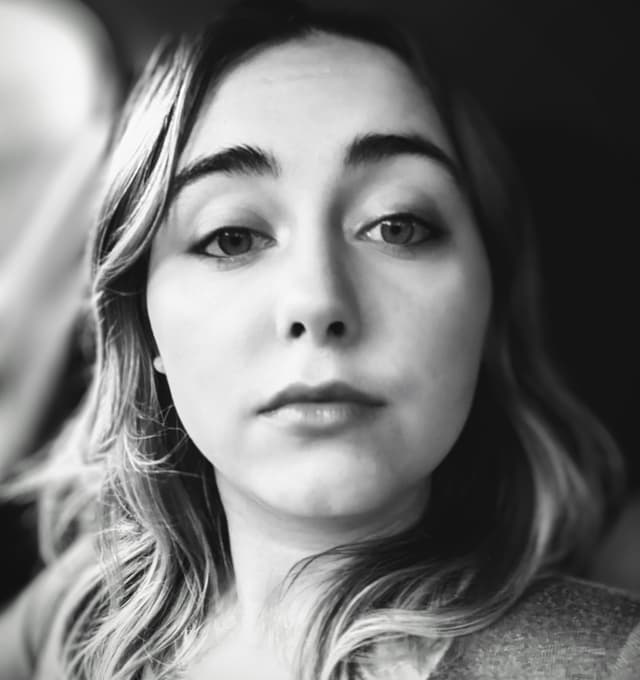 A black and white portrait of a young woman with wavy hair and a pensive expression, set against a blurred background.