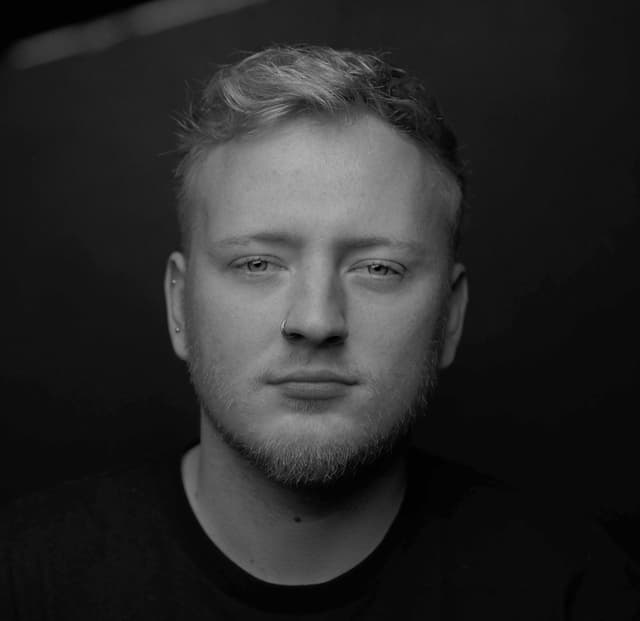 A black and white portrait of a man with a serious expression, his face illuminated against a dark background.