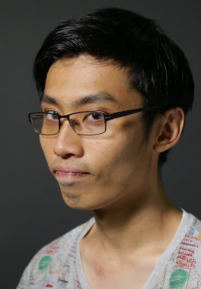A young man with short dark hair and glasses, wearing a white shirt, appears against a dark background.